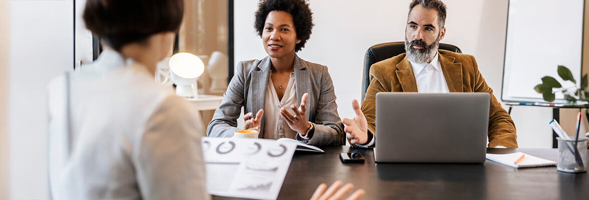 Two business people in suits listening to a presenter in a meeting room.
