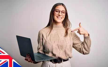 Smiling woman holding laptop in one hand and pointing to it with other hand