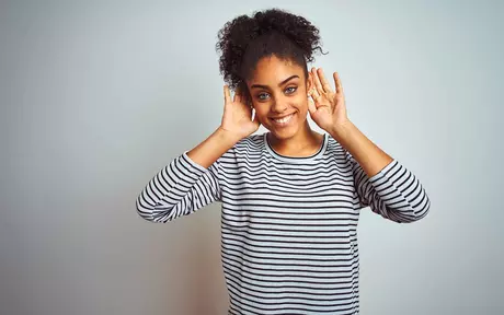 young woman smiling and holding her hands to her ears