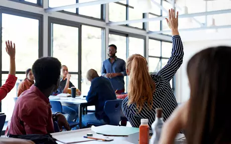 a university classroom with several students with their hands up